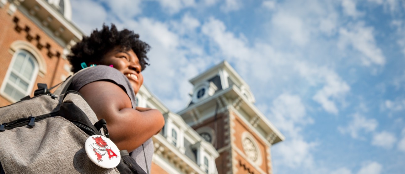 UARK Student with blue skies and Old Main in the background